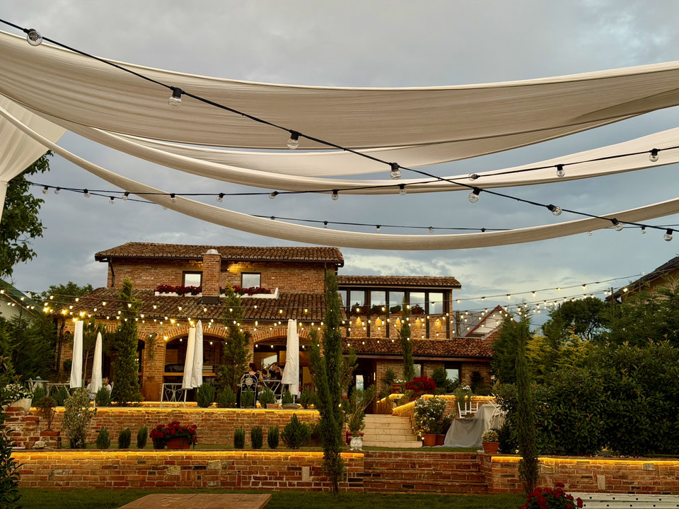 Terasa Ristorante Toscana la apus, cu ghirlande de lumini, mese și grădina cu chiparoși
